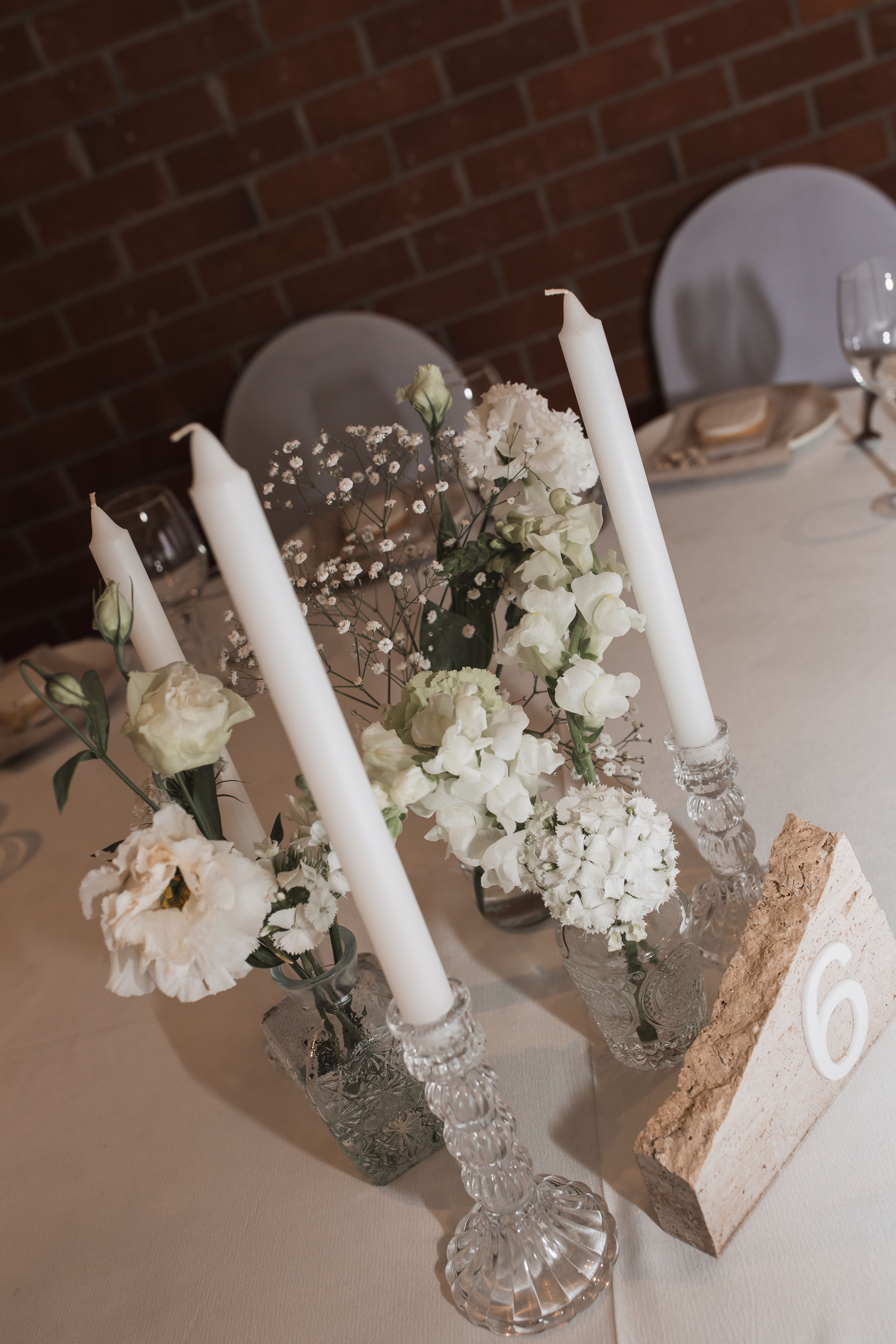 Elegant wedding table decor with white taper candles in crystal holders and delicate white floral arrangements.