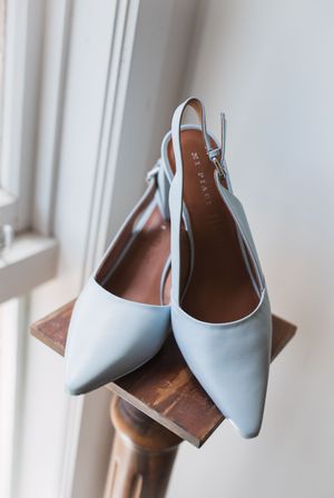 Light blue slingback kitten heels with pointed toes sit elegantly on a wooden ledge near a window.