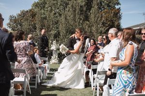 Wedding guests gather outdoors under shady trees during a sunny summer celebration.