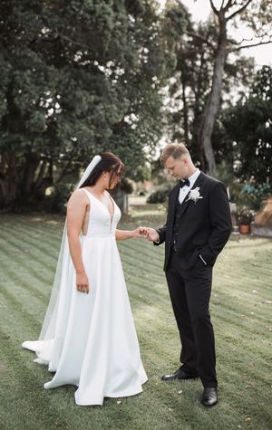 A couple in wedding attire shares a tender moment on a grassy hillside during their outdoor wedding photoshoot.