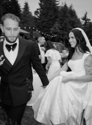 Black and white wedding celebration photo with string lights and evergreen trees.