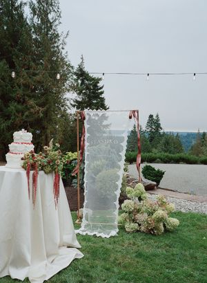 Elegant wedding dessert display with white tablecloths and floral arrangements on a grassy hilltop overlooking scenic views.