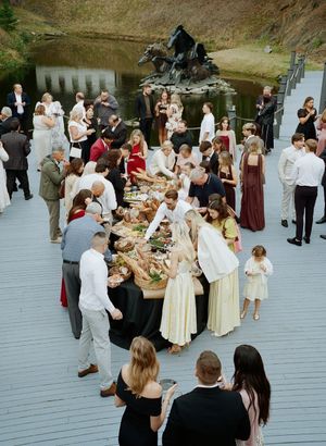 Overhead view of wedding reception with guests gathered around long table by waterfront.
