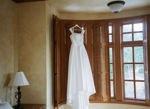 Wedding dress hanging in a sunlit room with wooden trim and multiple windows creating a romantic getting-ready scene.