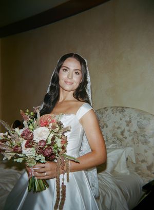 A bride in a white wedding dress holds a romantic bouquet with pink and burgundy flowers.