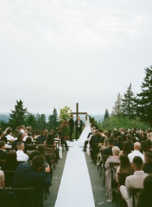 Outdoor wedding ceremony with white aisle runner and guests seated on both sides against mountain backdrop.