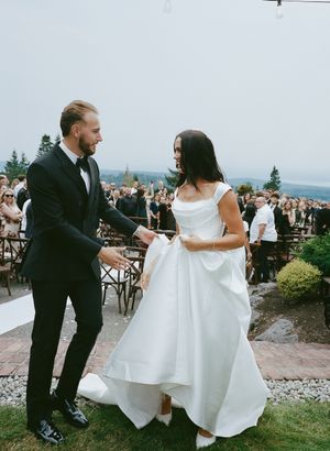 Wedding couple dances on outdoor terrace with mountain vista and reception guests in background.