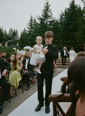 Wedding guests mingling and dancing on outdoor patio with string lights and evergreen trees.