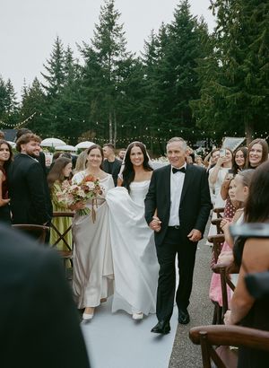 Wedding processional on white aisle runner with evergreen trees and string lights overhead.