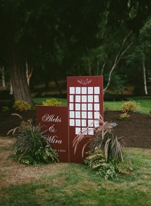 Wedding seating chart display with burgundy boards and greenery decorations in an outdoor garden setting.