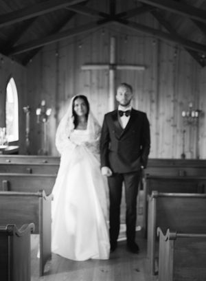 Wedding ceremony in rustic wooden chapel with arched windows and cross backdrop.