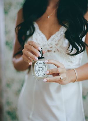 Close-up shots of hands holding a Diptyque perfume bottle in delicate lace wedding setting.