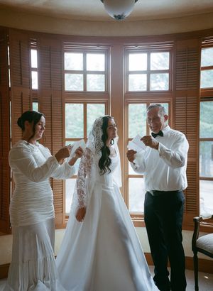 Wedding preparations in a sunlit room with wooden shutters and elegant white attire.