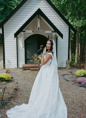 Elegant white chapel with flowering garden provides backdrop for bridal portrait.