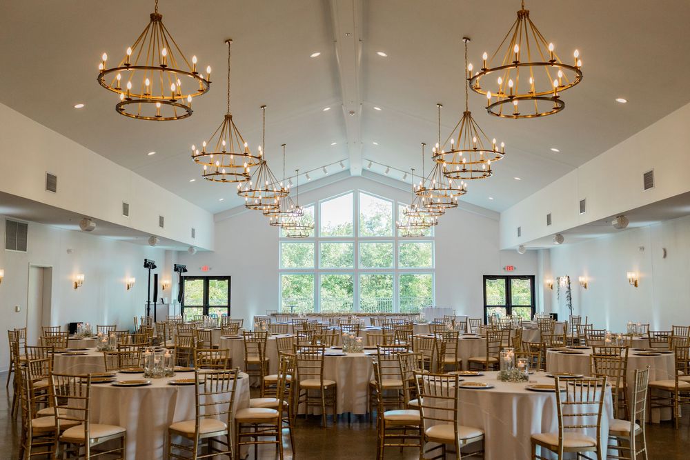 Elegant wedding reception venue with gold chandeliers, white walls, and rows of chiavari chairs set for a celebration.
