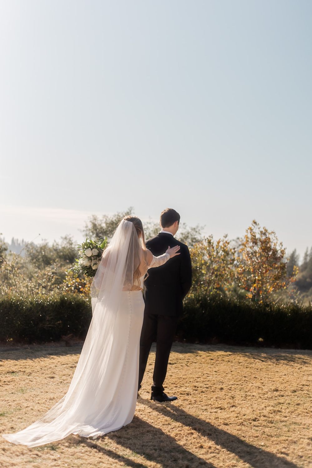 A romantic wedding couple embraces while looking out over a scenic overlook during golden hour.