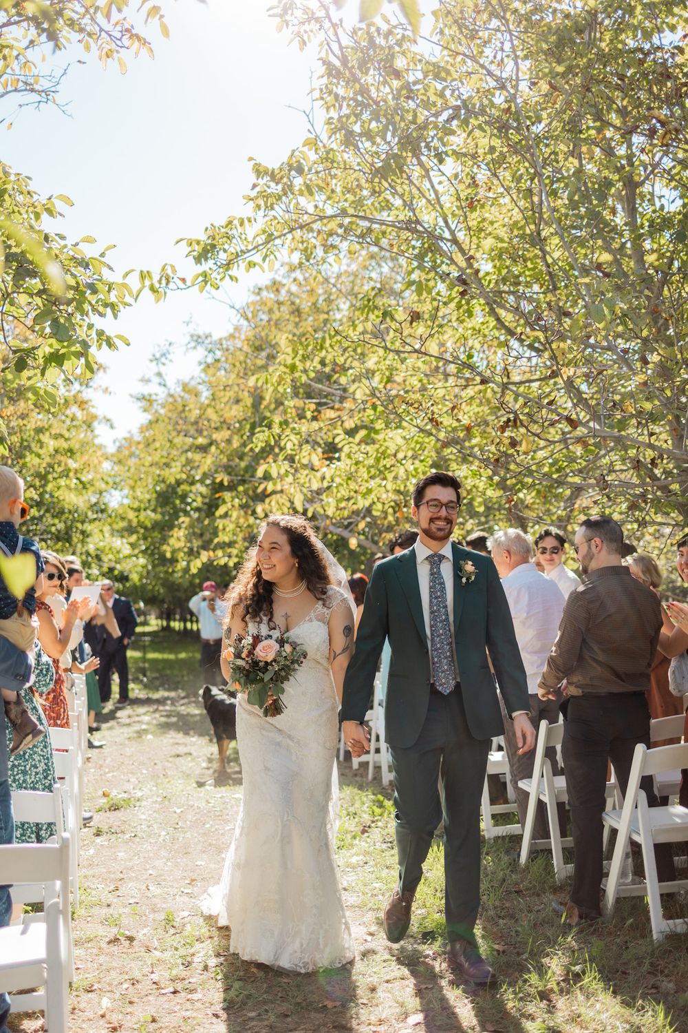 Outdoor wedding ceremony in an orchard with white chairs and autumn leaves scattered on the ground.