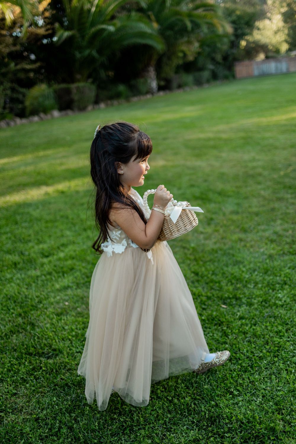 Two children in cream-colored dresses play together on a lush green lawn during golden hour.