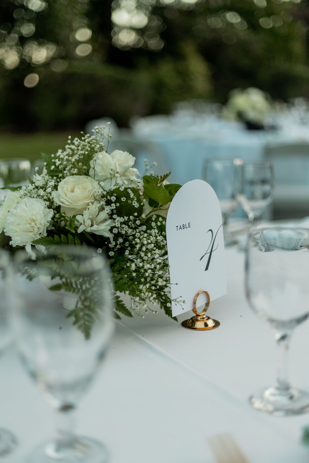 White floral centerpieces and table numbers decorate an elegant wedding reception table setting.