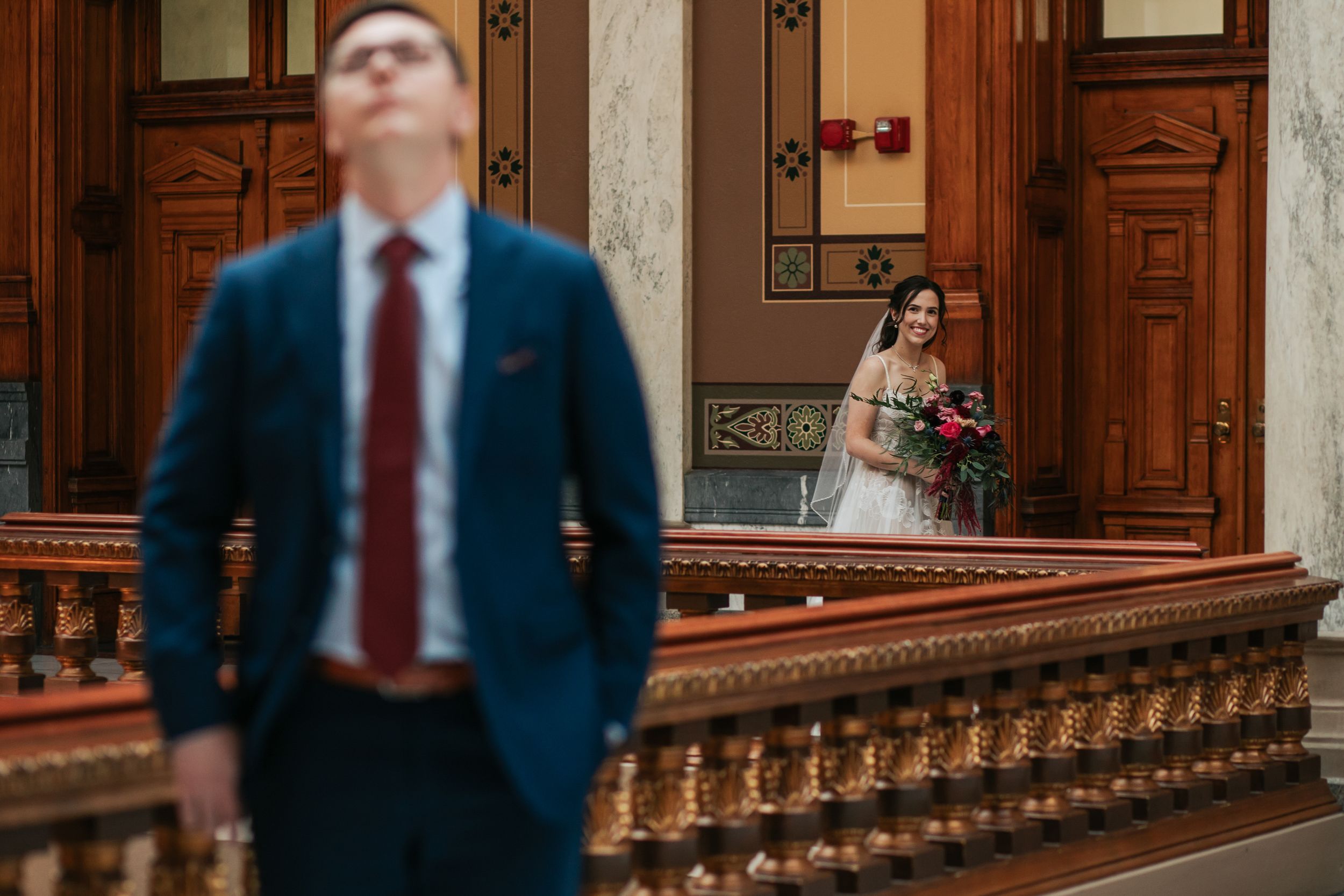 A person in a suit walks down an ornate wooden staircase in a grand historic building.