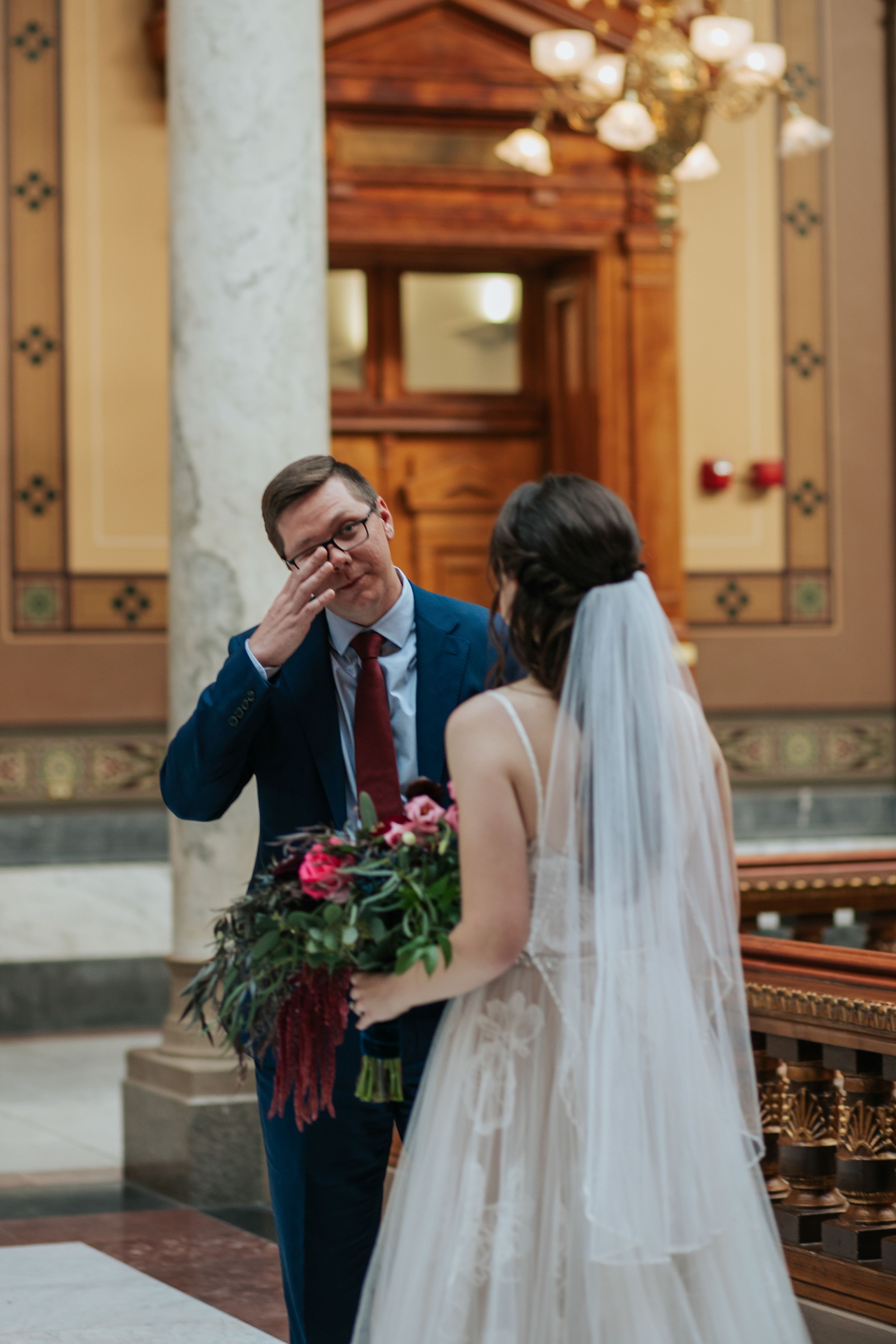 Bride and groom share an emotional first look moment in an elegant indoor venue with ornate architectural details.