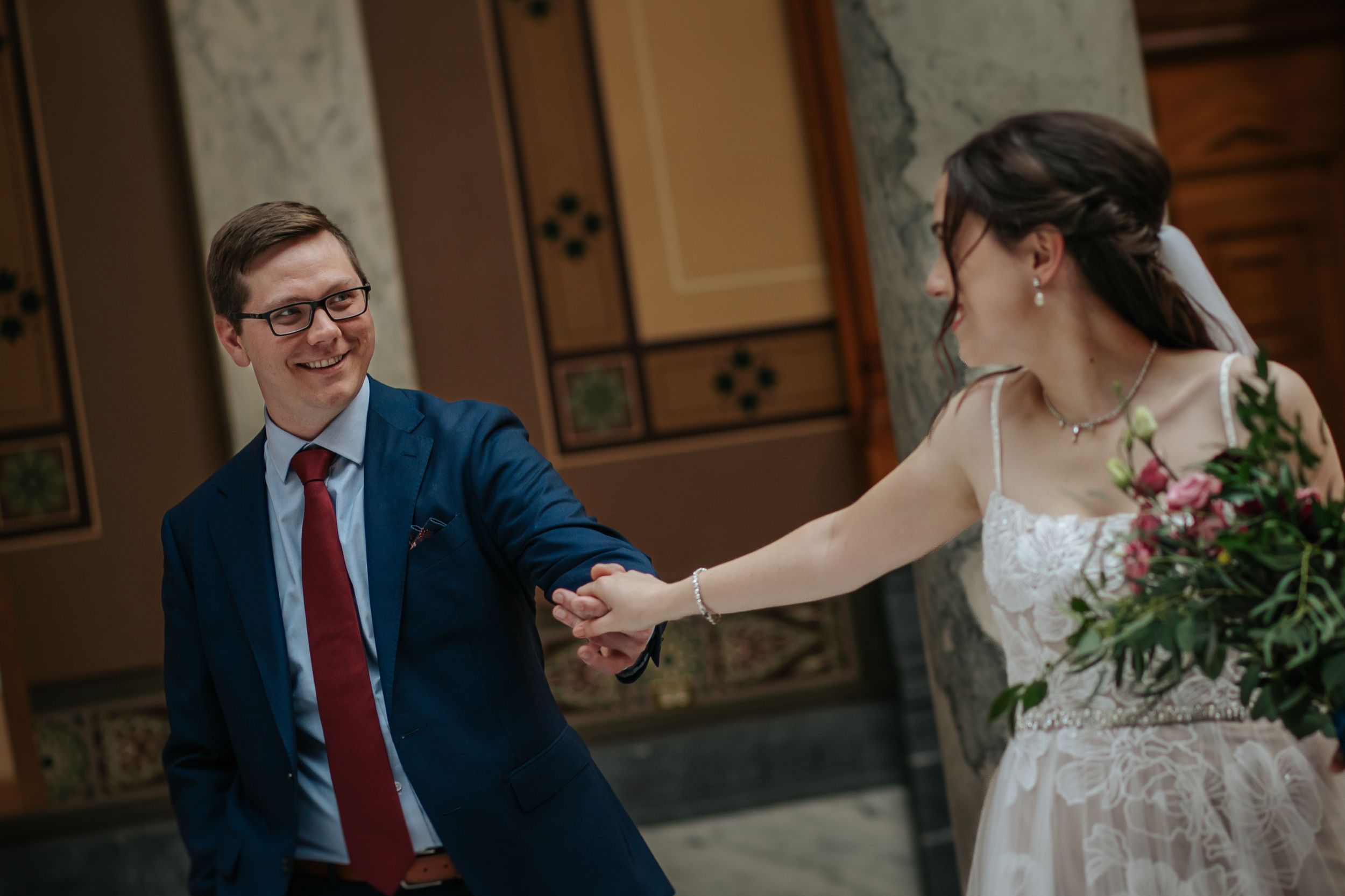 Couple embraces in an elegant indoor venue with ornate decor and warm lighting.