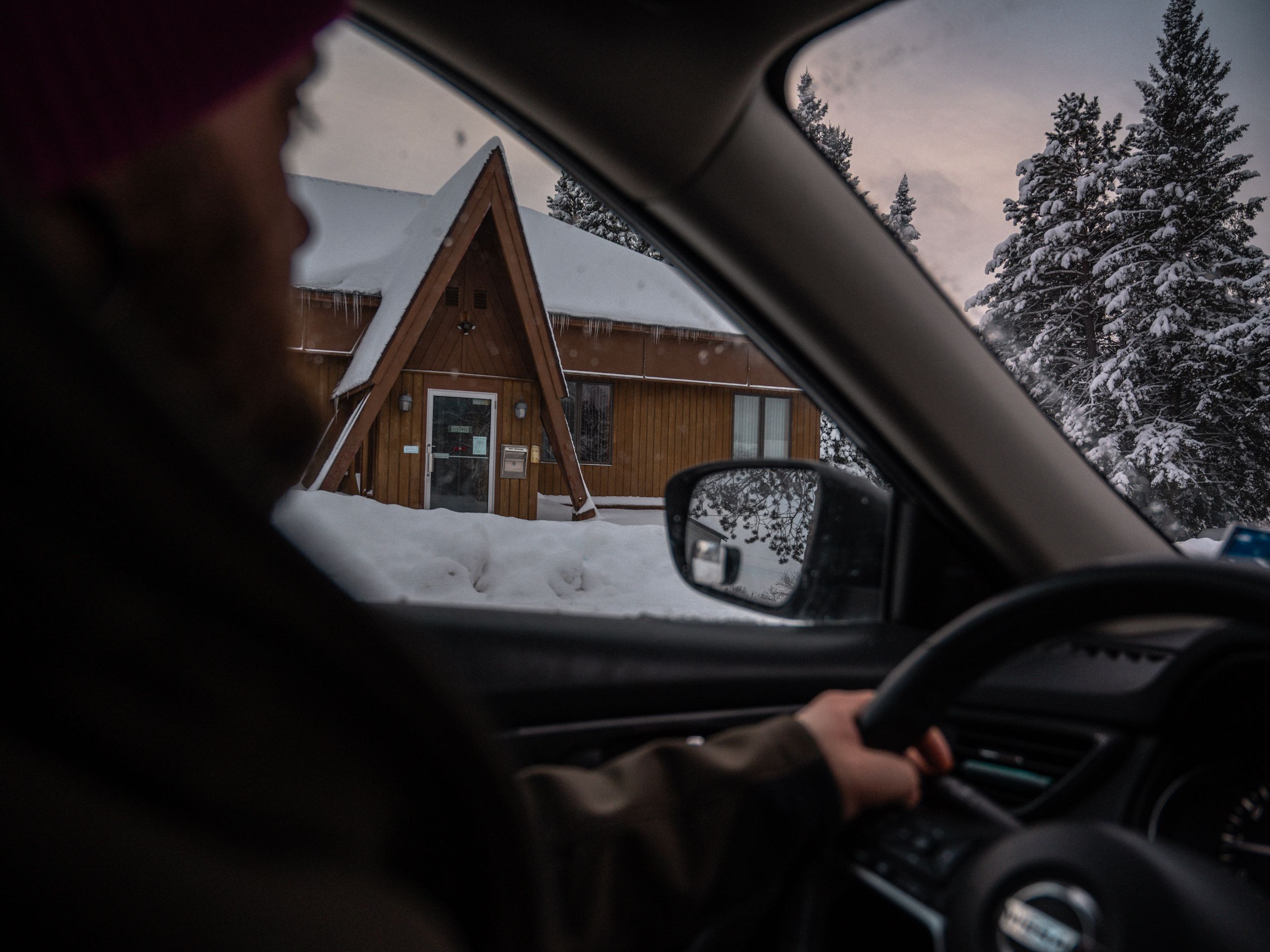 View of snow-covered cabin through car windshield while driving.