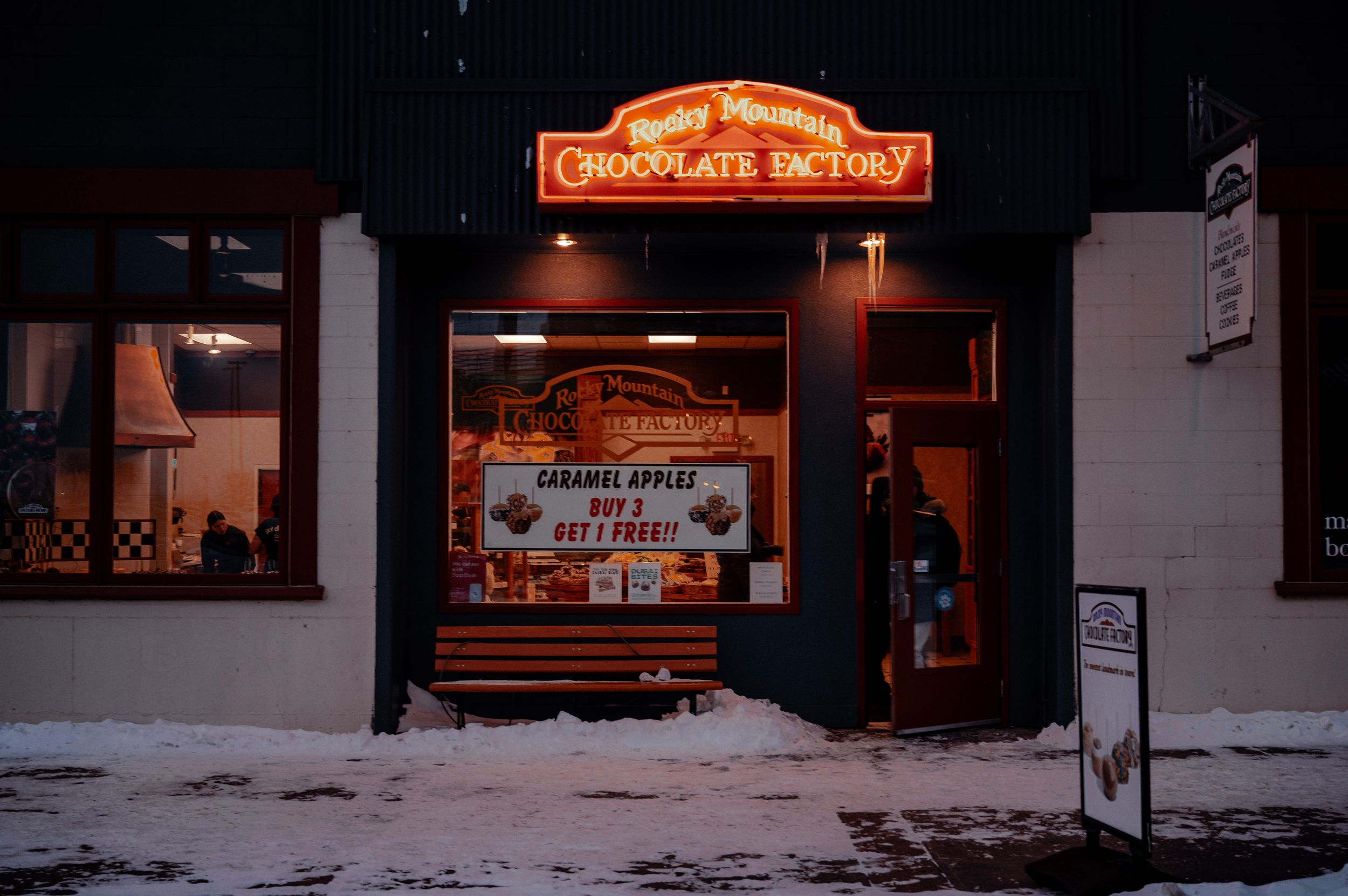 Illuminated chocolate factory storefront at night with neon signs glowing in the darkness.