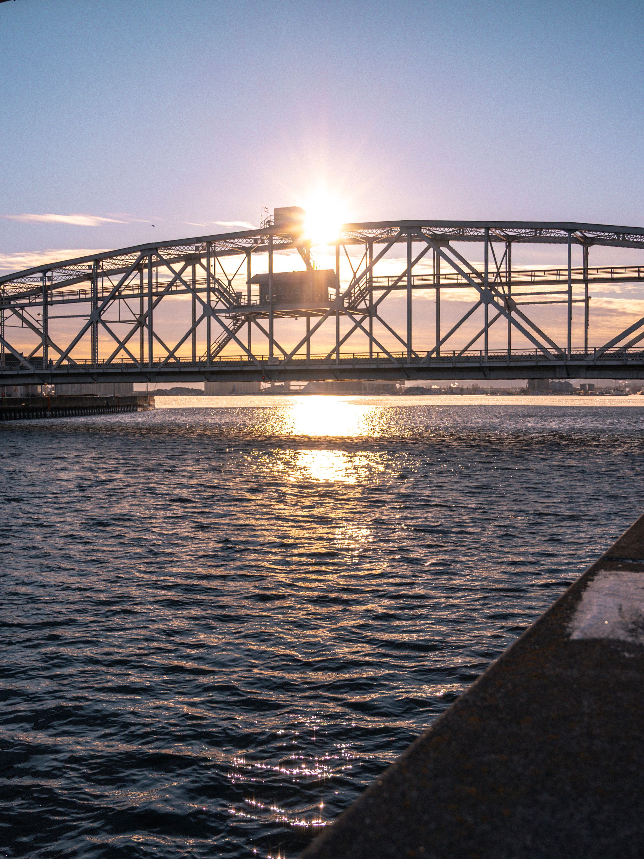 Steel bridge silhouetted against golden sunset over rippling water.