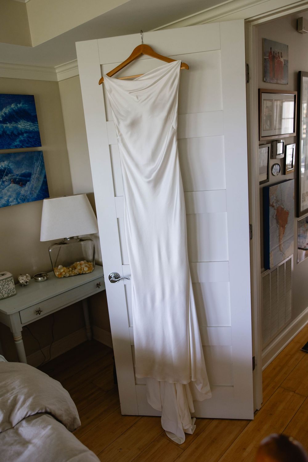 An elegant white wedding dress hangs on a door in a sunlit room. Weatherlow Farm wedding. Westport Massachusetts.