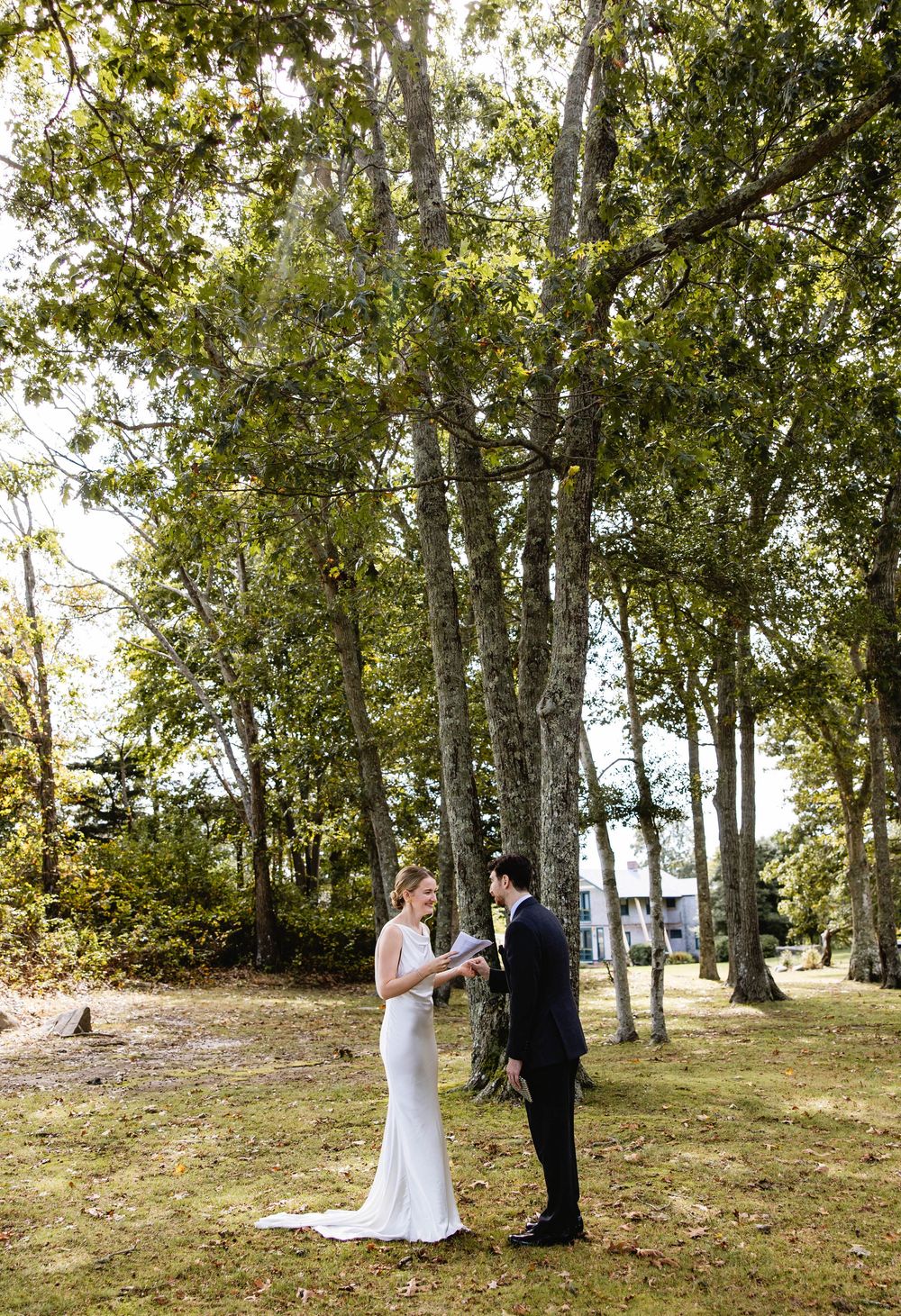 A wedding ceremony unfolds in a scenic wooded area with trees and natural lighting. Weatherlow Farm wedding. Westport Massachusetts.