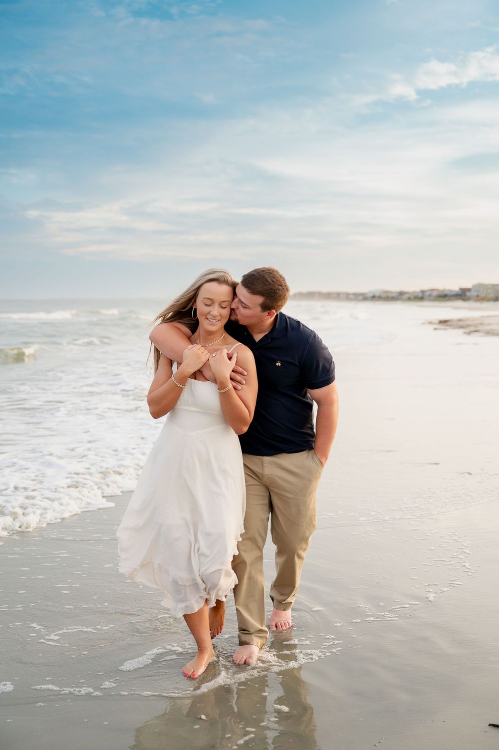 Couple playing and laughing together at water's edge during beach photoshoot.
