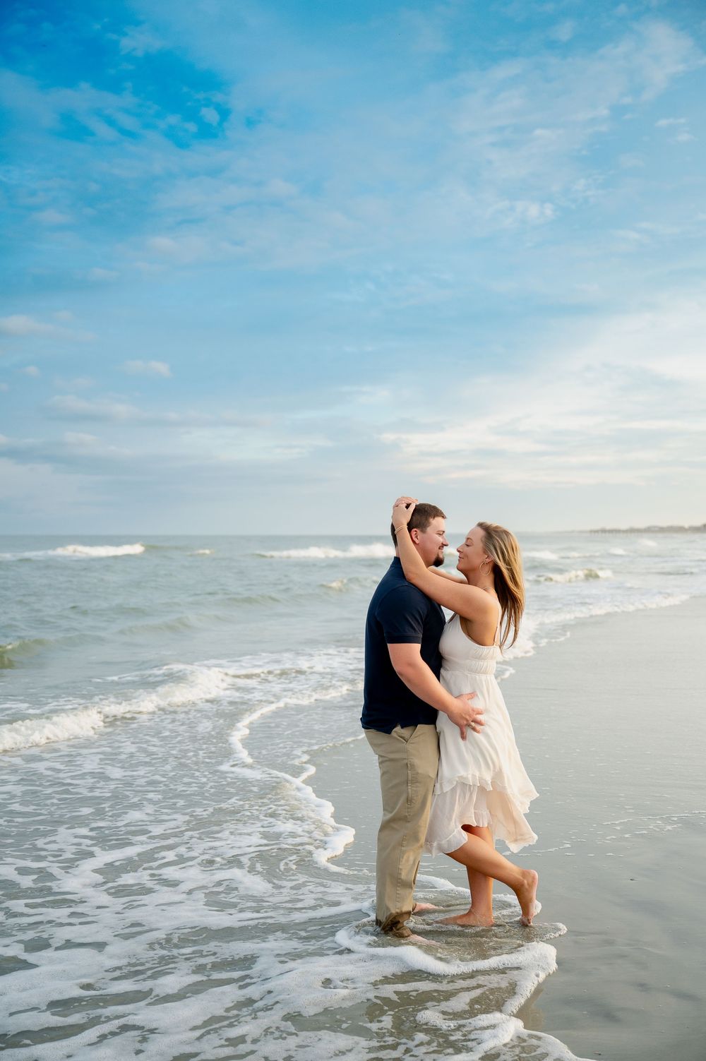 Romantic couple dancing and embracing in ocean waves during sunset beach photoshoot.