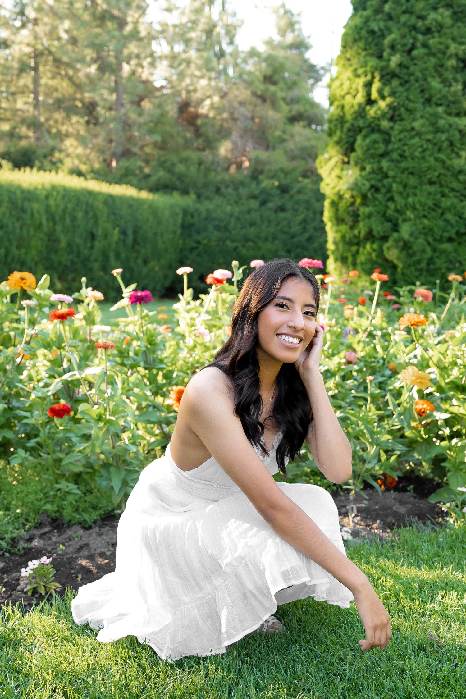 A series of four photos showing someone in a white dress laying in a garden with colorful flowers on a sunny day.