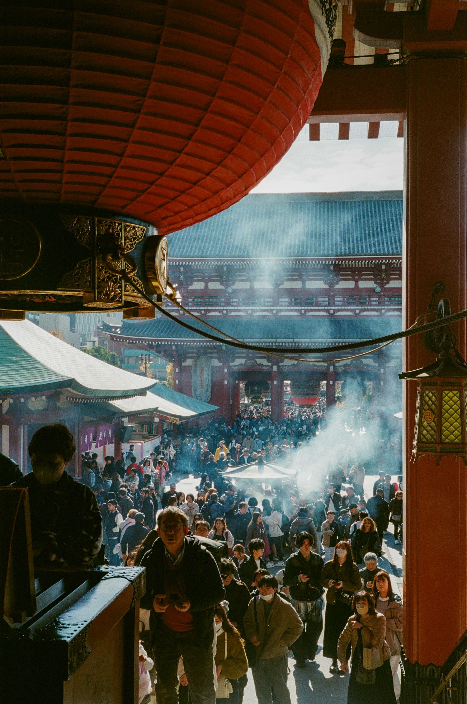 Crowded temple courtyard filled with incense smoke and red lanterns during a traditional ceremony in Japan.
