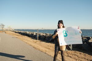 People holding signs stand on a coastal path with ocean views and rocky shoreline during daytime.