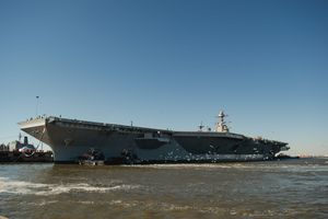 A panoramic view of a large aircraft carrier ship docked in calm waters under clear blue skies.