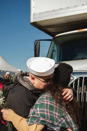 A sailor in dress whites embraces a loved one in an emotional homecoming reunion at a naval base.