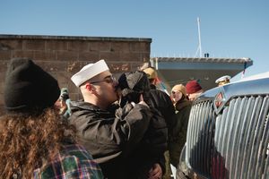 A group of people stand in line at an outdoor event against a blue sky backdrop.