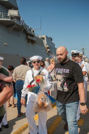 A group of people gathered on a naval vessel deck during what appears to be a homecoming celebration.