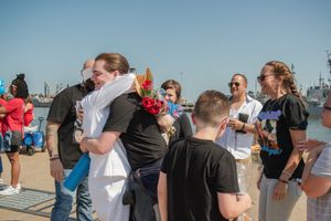 People gather on a pier or dock during a sunny day, with some embracing while others stand nearby.