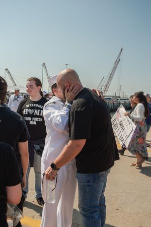 Group of people gathered at a port or dock area with cranes visible in the background.