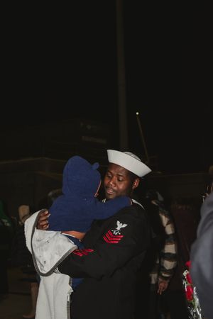 Service members share heartfelt hugs during a dark evening homecoming event.