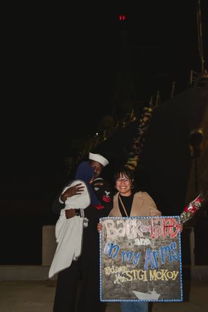 A group poses with a decorated sign at night while celebrating a special occasion.