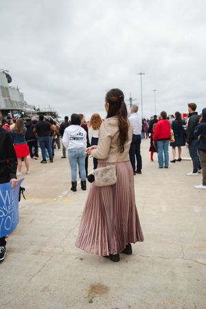 A group of people gathered on a pier or waterfront walkway with cloudy skies in the background.