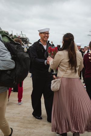 A group of people in formal attire gather on a dock during what appears to be a military homecoming event.