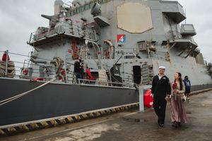 Military ship docked at port with sailors and family members gathered on deck for reunion.