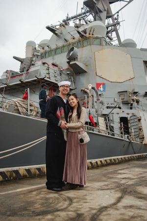 A naval ship serves as backdrop for an emotional reunion scene at a military port.