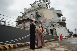 Naval vessel moored at dock with personnel and visitors visible on the deck during homecoming event.