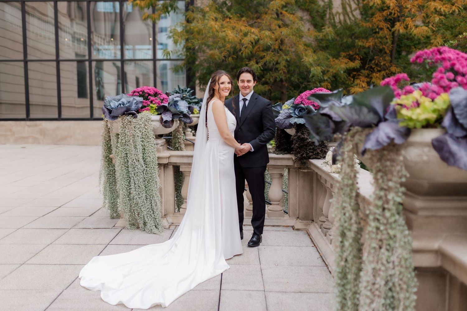 A couple walks along a garden path surrounded by blooming flowers and lush greenery during a wedding ceremony.